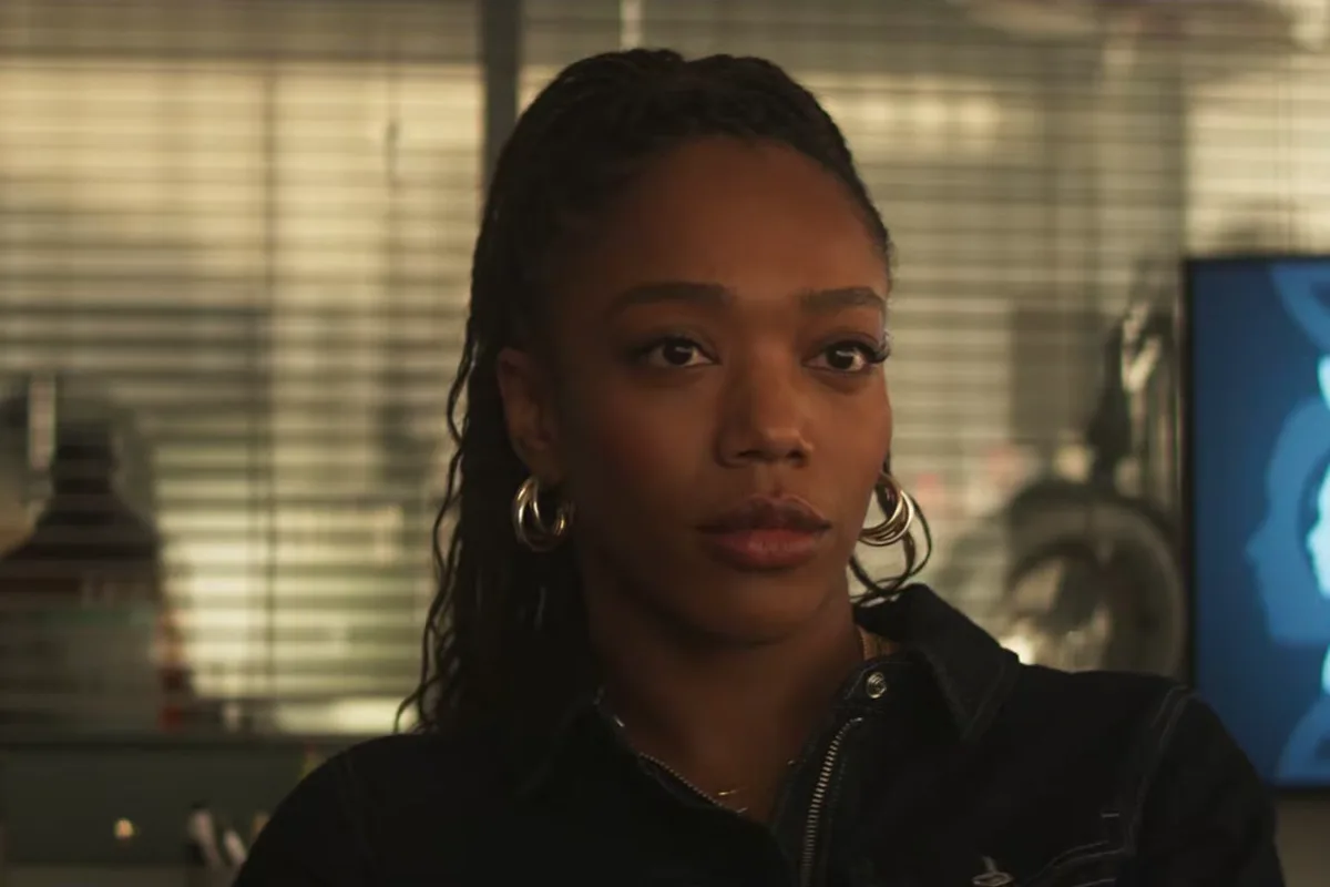 Naomi Ackie as Dr. Caitlyn Corr in her lab, with a DNA graphic on a screen behind her