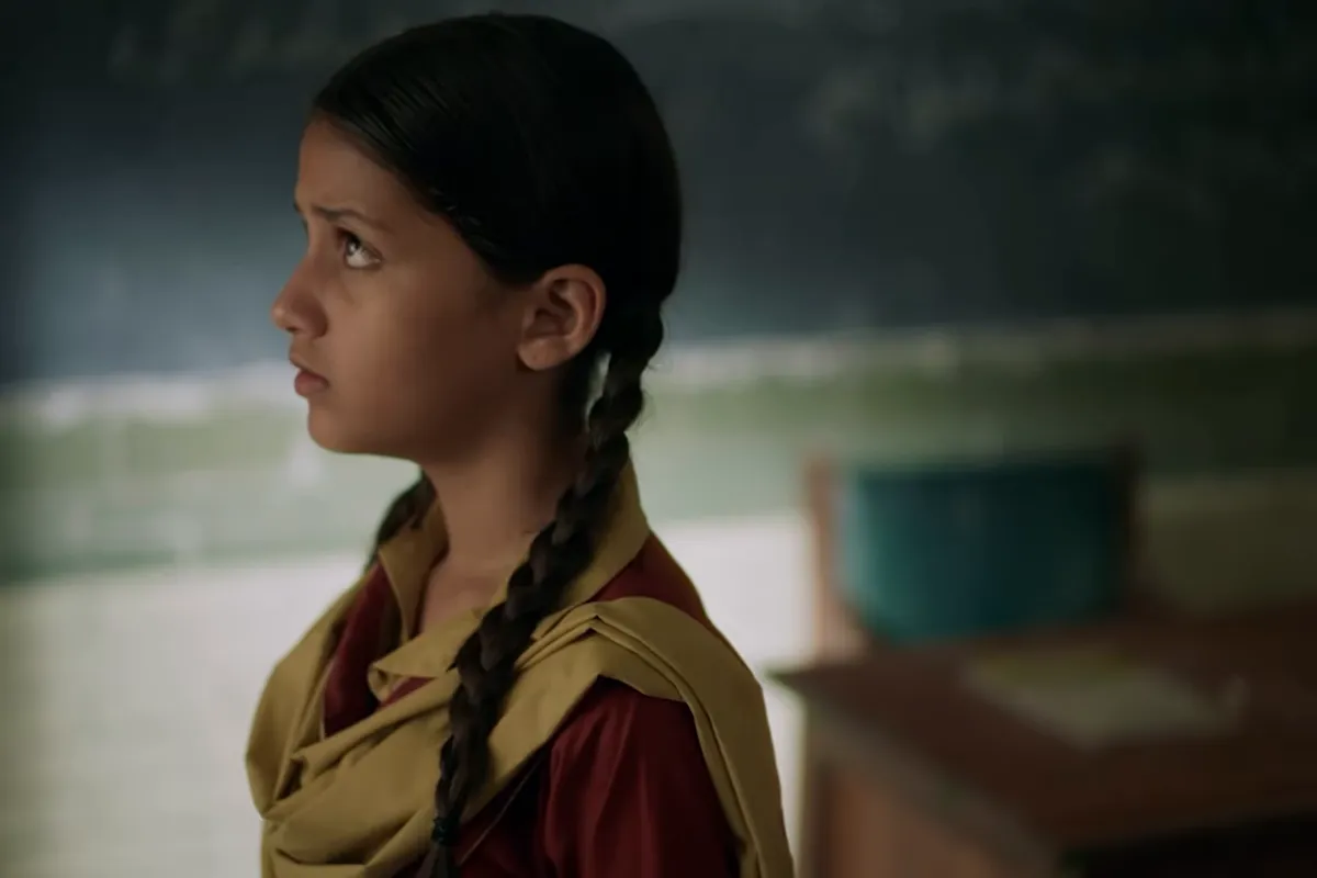 Rabia, in her school uniform with her hair in two plaits, looking up inside an empty classroom