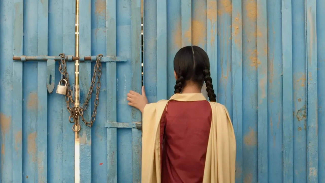 Nazualiya Arsalan as Rabia, in a maroon school uniform and yellow scarf, standing on a village street at night