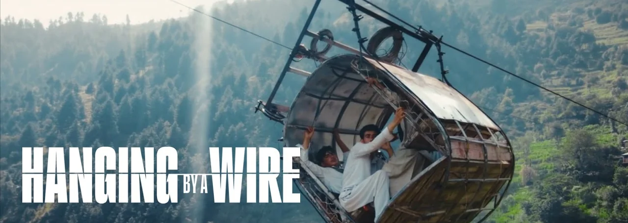 Hanging by a Wire key art: schoolboys inside a battered cable car suspended over a forested valley, with the film's title