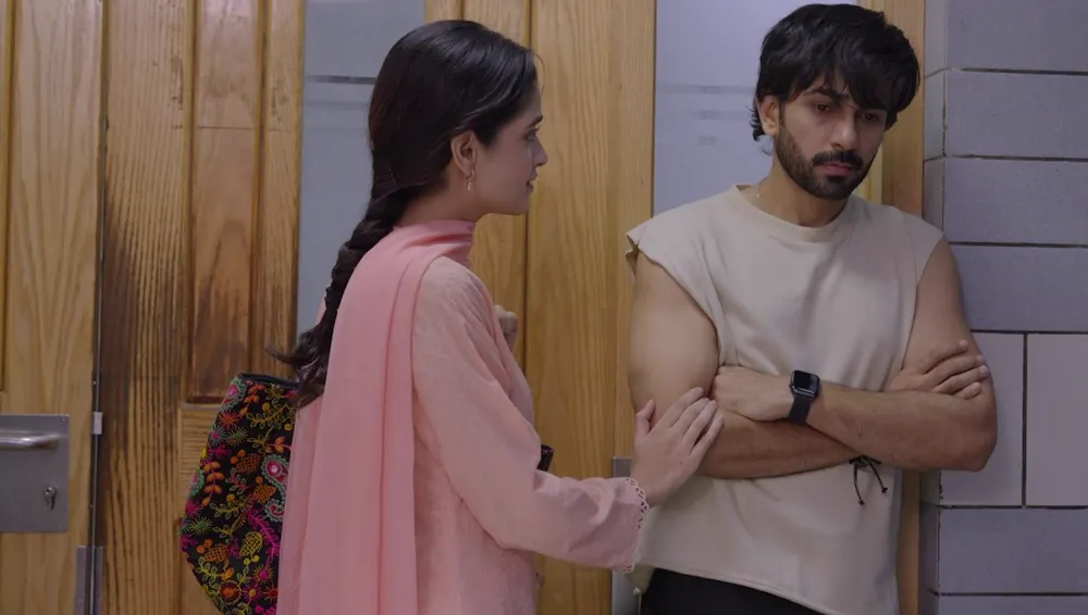 A young woman in pink touching the arm of a man in a sleeveless top who stands with his arms folded