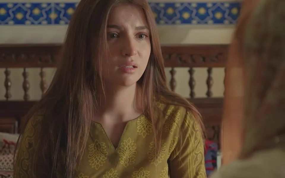 Dananeer Mobeen as Hurmat, in a green kurta, looking worried in a room with a carved wooden bed