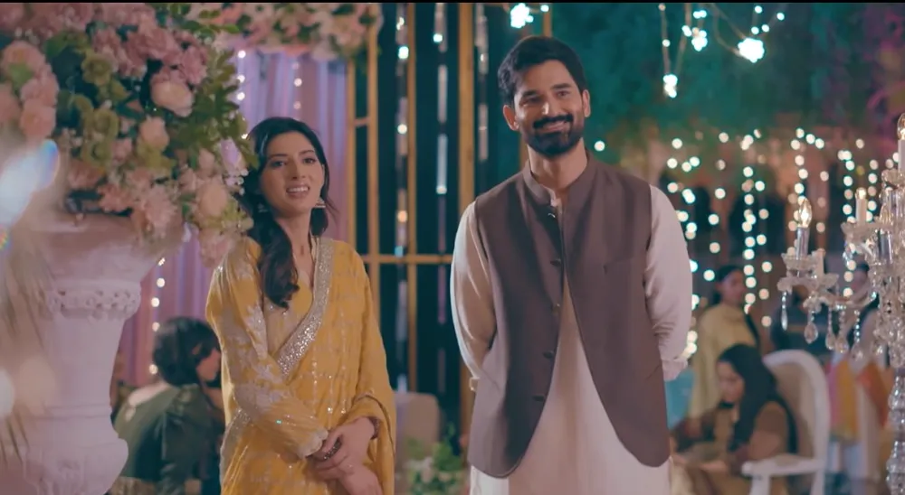 A woman in a yellow outfit and a smiling bearded man in a brown waistcoat at a wedding lit with fairy lights