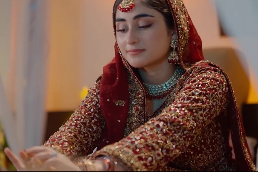 A bride in a red embroidered dupatta and turquoise necklace sitting alone, eyes lowered